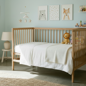 Wooden cot with white mattress cover and bedding in a nursery with light blue walls and accessories 