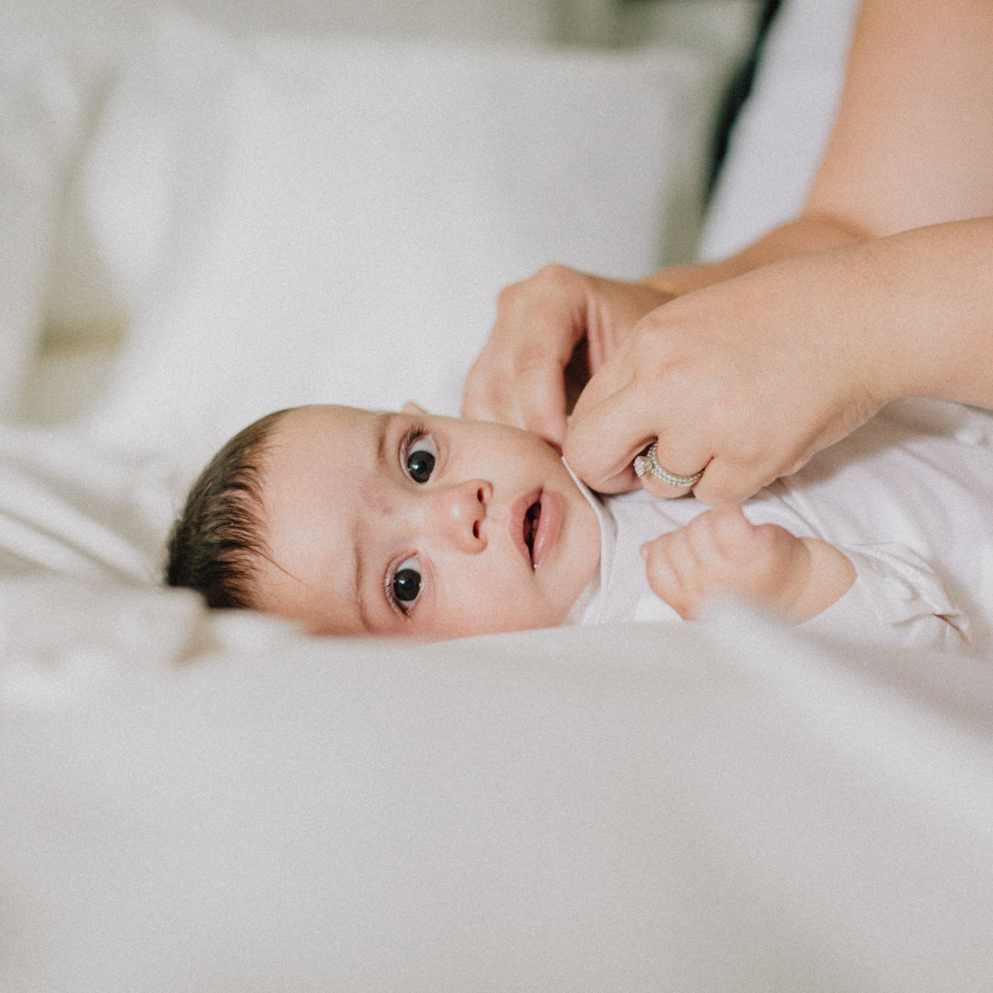  Relaxed baby lying on white bedding, looking at camera 