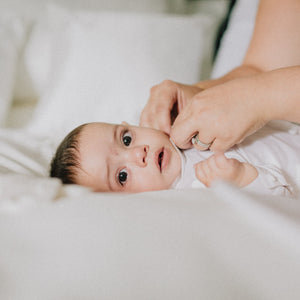  Relaxed baby lying on white bedding, looking at camera 